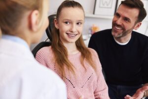Smiling girl with braces and her father talking with the orthodontist