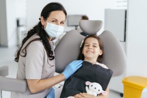 Pediatric dentist smiling with a young girl in the dental chair